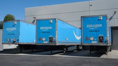 Three blue Amazon delivery trucks at bays at a distribution center