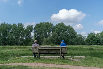 Two friends sit and talk at a social distance in Fletcher Moss park, Manchester, UK