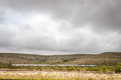 Amtrak Sunset Limited train viewed from the side passing low desert hills in West Texas