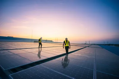 Solar panels on a rooftop with two workers in hard hats and safety vests walking between panels
