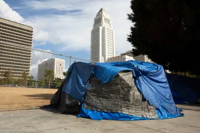 A tent covered in blue and black tarps sits on a downtown Los Angeles sidewalk with the white ziggurat-topped L.A. City Hall looming in the background