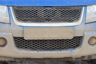 Close-up of license plate on blue car covered in mud, license plate is unreadable.
