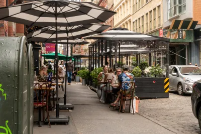 New York City sidewalk with outdoor dining patio with black and white striped umbrellas and black barriers protecting diners from traffic