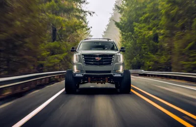 Cadillac Escalade SUV driving toward camera on black asphalt road surrounded by forest