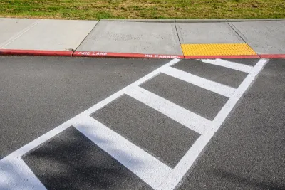 Freshly painted white crosswalk leading to yellow curb cut to sidewalk