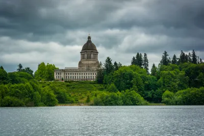 View of Washington state capitol building dome from across lake with green trees in foreground and grey cloudy sky