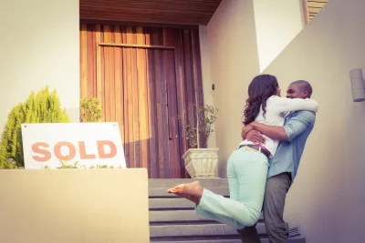 Couple embracing happily in front of home with "SOLD" sign