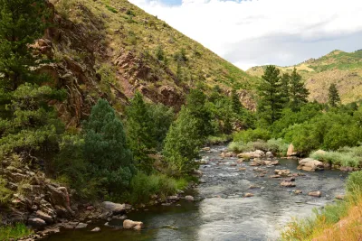 Shallow river with tree-lined banks and hillsides in the background