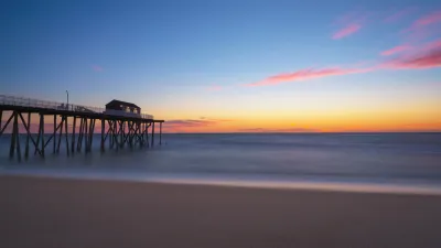 View of empty beach with wooden fishing pier going out into Atlantic Ocean at sunset in New Jersey