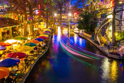 View of San Antonio River Walk with colorful umbrellas at tables on waterfront and with boat lights blurred by long-exposure