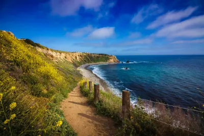 Dirt walking trail with blue ocean on one side and green hillside on the other in Rancho Palos Verdes, California