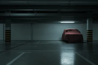 Dark parking garage, empty except for one car covered with a red tarp