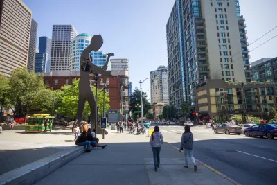 People walking on a sidewalk in front of the Seattle Art Museum, which have the hammering man and a skyscraper in the background, Washington, USA