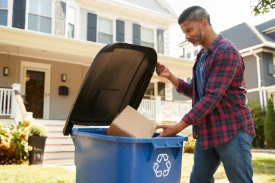 Man dropping cardboard box in blue curbside recycling bin