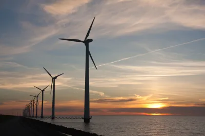 Line of offshore wind turbines with sunset over sea in the background