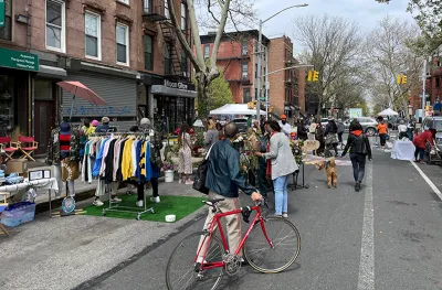 Man with red bicycle walks bike down 'open street' with vendor booths in New York City.