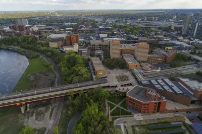 University of Minnesota Humpharey primary image of the city scape, a body of water on the left side, and a bridge running across the lower half of the image.