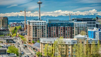 View of multistory buildings under construction in downtown Seattle, Washington with Space Needle and Mount Rainier in background.