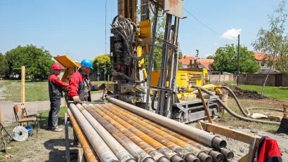 Workers next to excavator digging a geothermal well.