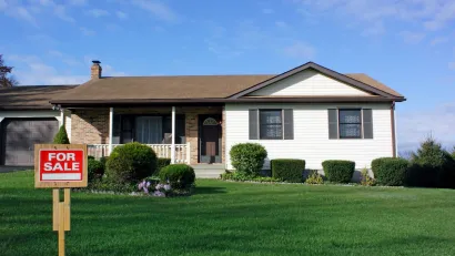 Small home with For Sale sign on green lawn.