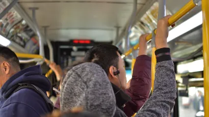 Interior of busy city bus with people standing, holding on to top bar.