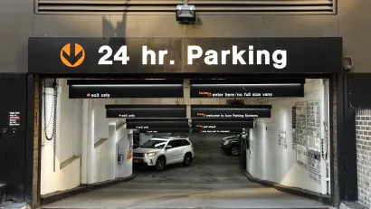 24-hour parking sign above parking garage entrance through which you can see a white SUV driving