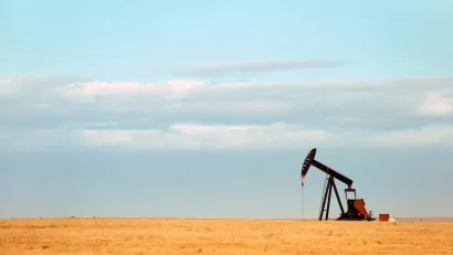 Single oil derrick on dry prairie with faded blue sky in background.