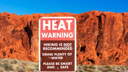 Extreme heat warning sign outdoors with red desert rock cliff in background.