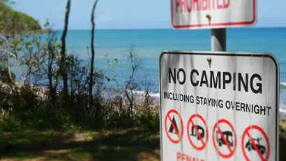 "No Camping" sign with symbols on a beachfront.