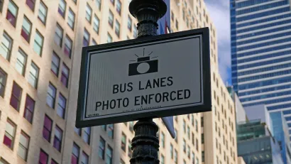 Close-up of "Bus Lanes - Photo Enforced" sign with camera logo on New York City street pole.