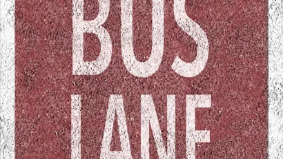 Overhead view of white BUS LANE sign painted on red background on concrete street.
