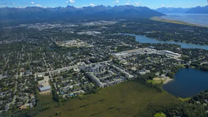 An aerial view of the Anchorage metropolitan area shows sprawling development surrounded by tall mountains.