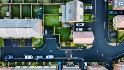 A suburban street in England, shown directly from above, with lush, green yards and driveways with cars parked in front.