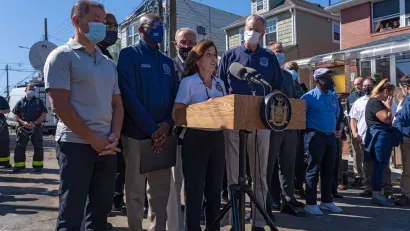 New York politicians, including Governor Kathy Hochul and Mayor Bill de Blasio, gather in front of microphones for a press conference.