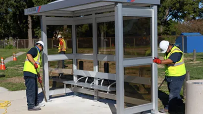 Workers in yellow safety vests installing a bus station shelter in Houston, Texas.