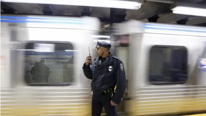Transit police officer standing on subway platform with blurred train passing behind him.