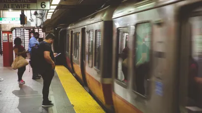 Passengers on Boston subway platform with blurred speeding train passing by