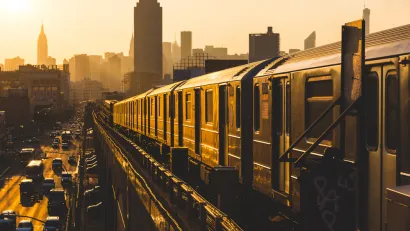 Golden sunset view of New York City subway train on elevated track with Empire State Building in background