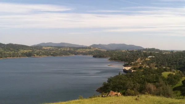 A large reservoir and its dam are shown in golden foothills.