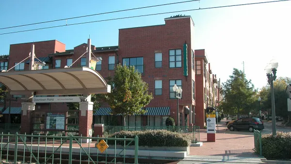 Above-ground downtown Plano train stop in front of red brick multifamily housing building.