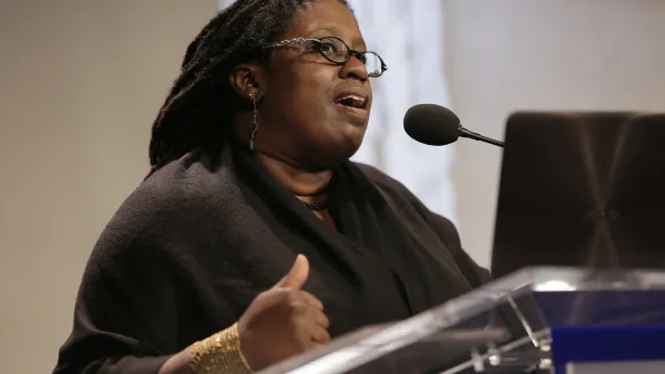 Black woman speaking at podium with presentation screen in background.