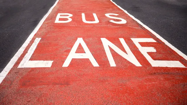 Close-up of red and white BUS LANE sign painted in street lane.