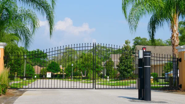 Closed black wrought iron gate in front of gated residential community with large palm trees along sides of street.