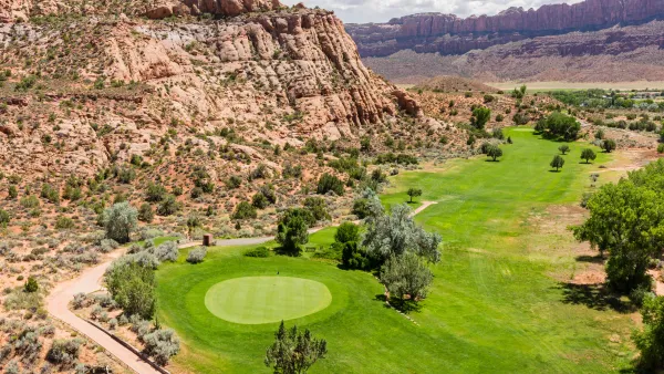 Aerial view of green colf course next to rocky desert cliffs in Moab, Utah