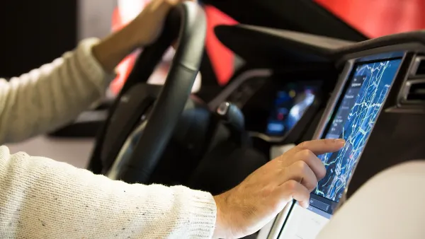 Close-up of man's hands on steering wheel and digital screen in Tesla car's driver's seat.