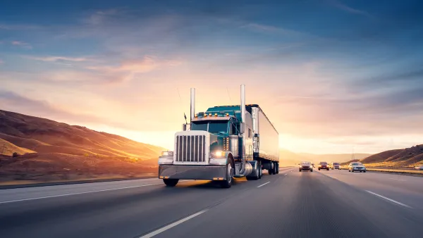 Semi truck driving down freeway with twilight sky in background.
