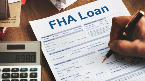 Close-up of hand filing out FHA Loan application on desk with calculator next to paper.