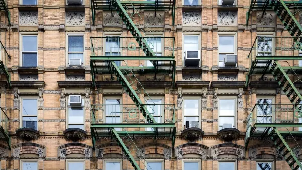 Brick New York City apartment building exterior with fire escape stairs and AC window units.
