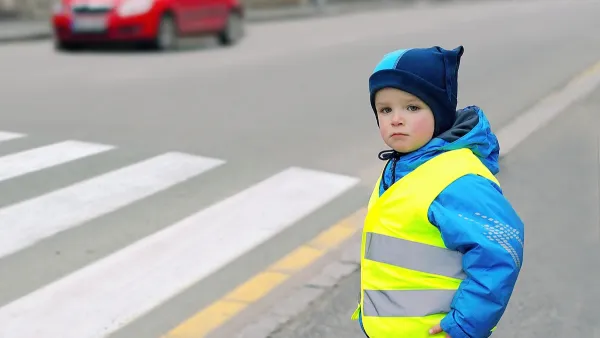 Child wearing yellow reflective safety vest looking before crossing street.