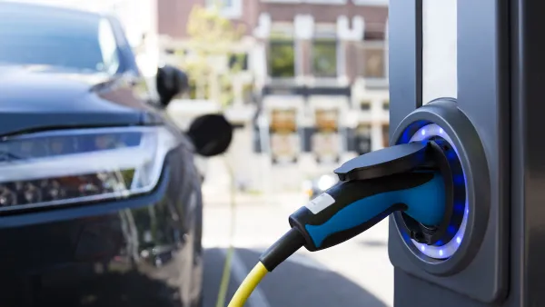 Close-up of electric car charging port with blurred dark colored car in background.
